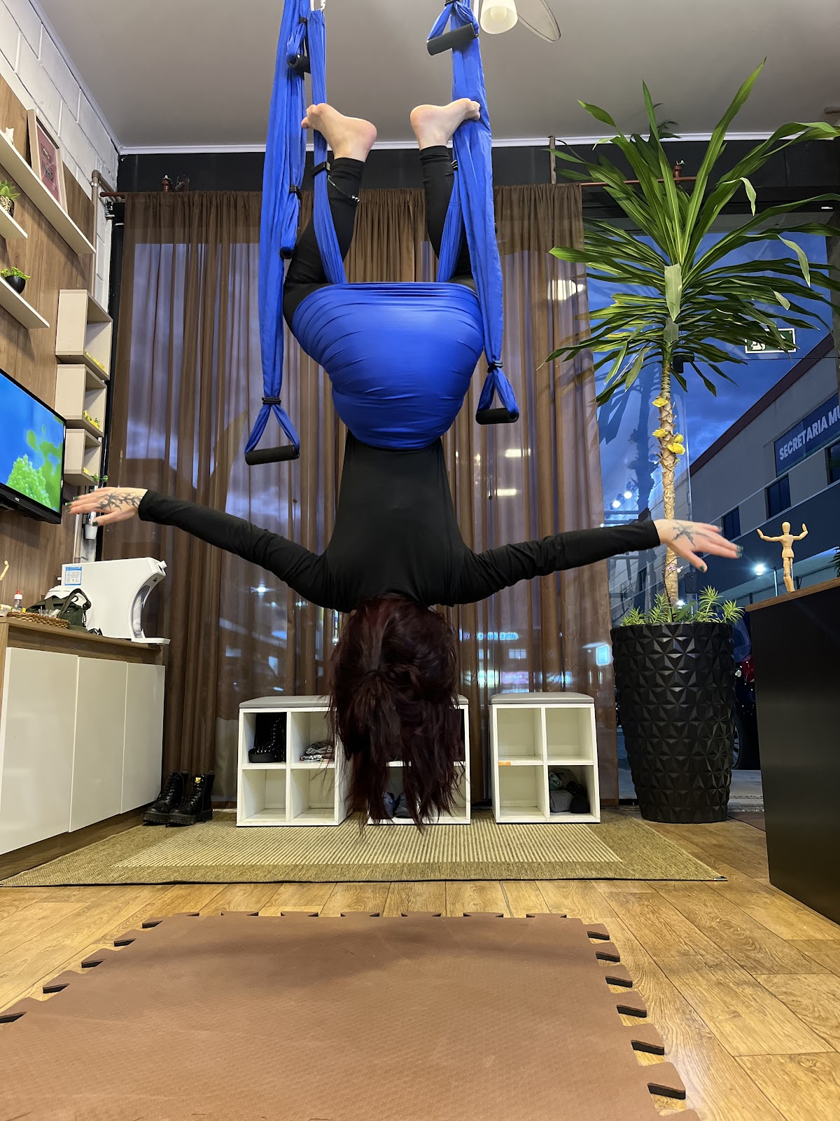 Aluna praticando Pilates aéreo no tecido azul, com braços abertos